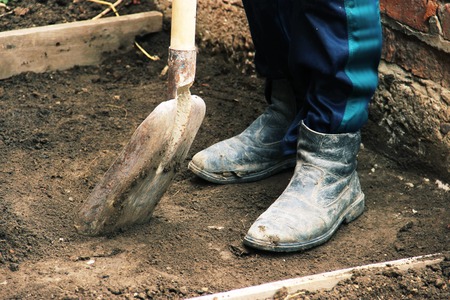 Install the formwork and remove the top layer of the ground by digging a pit or trench. Independent concreting of the site or track. A man in dirty shoes is digging a shovel.の写真素材