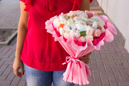 The original edible bouquet of marmalade, marshmallow in woman's hand. White and pink bouquet of food. Original handmade gift for a girl or child. Craft backgroundの写真素材