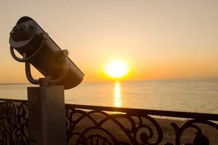 Binoculars on the coast of the sea. Tourist telescope on a background of sunset on the waterfront. Summer.の写真素材