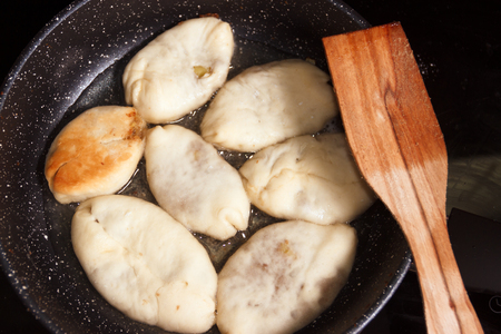 Meat pies, pan-fried in boiling oil. small raw pies in a frying pan with hot oil. wooden spatula.の写真素材