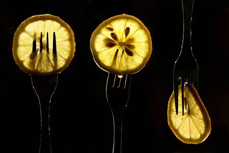 collage of three slices of lemons on the fork on dark black background. silhouette of a fork in the back light. Drops of juice flow down the forks.の写真素材