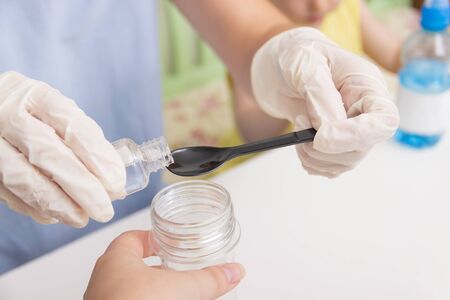 Hands in medical gloves pour liquid into a large plastic flask with a black spoon. How to make a...