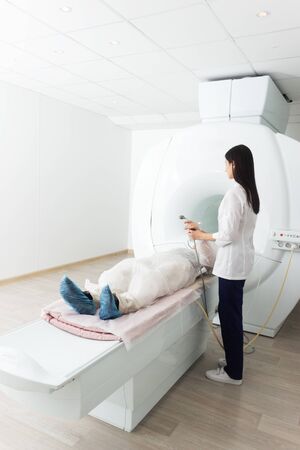 Radiologic technician and man patient lying on a CT Scan bed. preparing for MRI magnetic resonance imaging in a hospital. a nurse holds in hands and holds out to the patient call buttonの写真素材