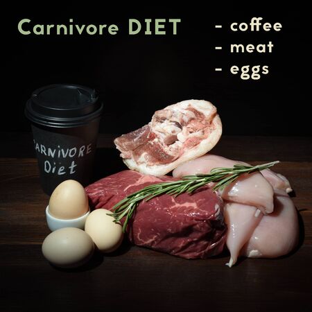 carnivore keto diet flat lay. coffee eggs, beef steak, chicken breast and pork shank assorted meat near a board made of natural stone. what to eat on carnivore diet text.の写真素材