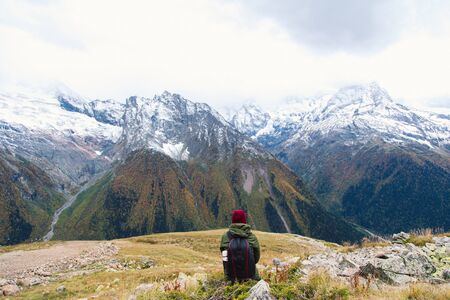 Travelling girl is sitting with backpack and  enjoying the beautiful view with snowy mountains in...