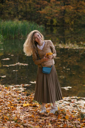 Young smiling blonde woman holding yellow leaves of maples in hands and walking in beautiful golden autumn park.の写真素材