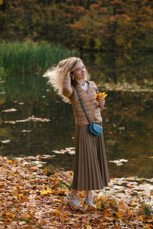 Young smiling blonde woman holding yellow leaves of maples in hands and walking in beautiful golden autumn park.の写真素材