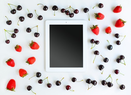 Tablet, cherry and strawberry on white background. Flat lay of working place. Mock up for art workの写真素材