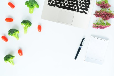 Workplace with broccoli, tomatoes, flowers and notebook with laptop. Top View isolated on white background. Vegetarian flat lay. Mock up for art works, blogs culinary, websites, social media.の写真素材