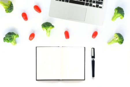 Workplace with broccoli, tomatoes and notebook with laptop. Top View isolated on white background. Vegetarian flat lay. Mock up for art works, blogs culinary, websites, social media.の写真素材