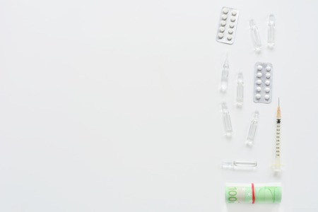 Medical composition with syringe, pills, ampules and money on white background. Top view of doctor workplace. Vertical flat lay mock up.の写真素材