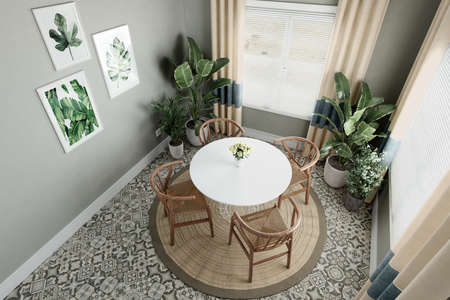 Gray wall above wooden table and chairs in bright dining room interior with lots of plantsの写真素材