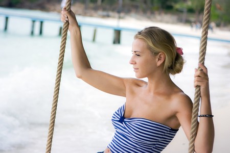 Pretty girl swinging on rope swings on the beachの写真素材