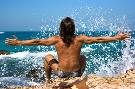Young man sitting on the rocky beach with splashesの写真素材