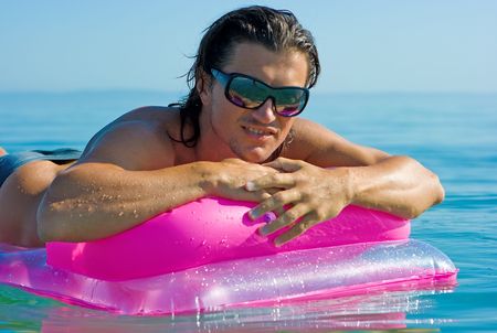 Handsome muscular young man floating on inflatable raft in sea water