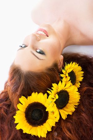 Close-up beautiful luxury fresh bright young lady in studio shot with sunflowers in her red long hairの写真素材
