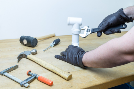 Caucasian hands in brown leather gloves fixing a pipe with a wrench on a working bench with tools spread all aroundの写真素材
