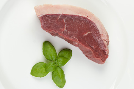 Slice of raw cow beef with some basil leaves isolated in white background - close upの写真素材