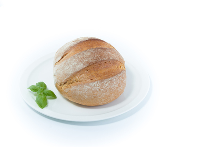 Full rustic loaf of bread with basil leaves on a white dish isolated on white backgroundの写真素材
