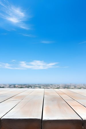 Empty wooden table with blue sky background. Perspective brown wood floor over blurred city viewの素材