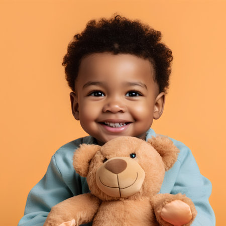 smiling african american boy holding teddy bear and looking at camera isolated on orangeの素材