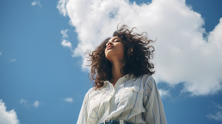 Portrait of a beautiful young woman with curly hair against the skyの素材
