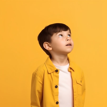 Portrait of a cute little boy on a yellow background looking upの素材