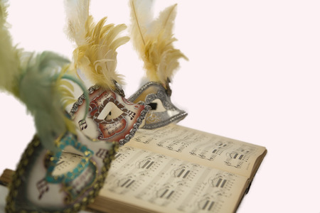 Three colorful carnival venetian mask with feathers on an open musical book.の写真素材