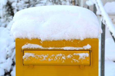 Yellow post box covered with a thick layer of snow.の写真素材