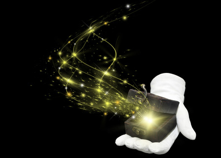 magician hand in white glove holding opened antique box with a yellow magic blown from inside