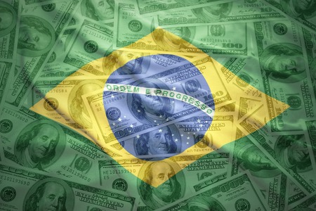 colorful waving brazilian flag on a american dollar money backgroundの写真素材