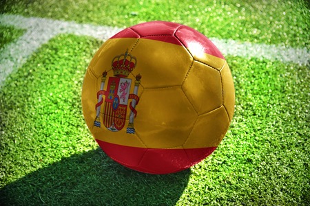 football ball with the national flag of spain lies on the green field near the white lineの写真素材