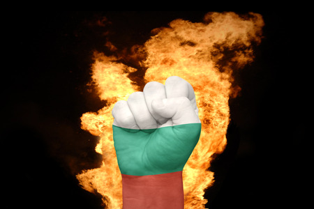fist with the national flag of bulgaria near the fire on a black background