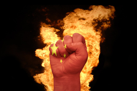 fist with the national flag of china near the fire on a black backgroundの写真素材