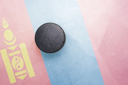 vintage old hockey puck is on the ice with mongolia flag