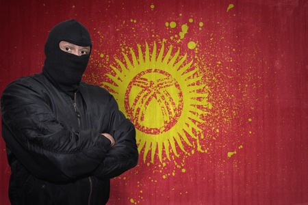 dangerous man in a mask standing near a wall with painted national flag of kyrgyzstan
