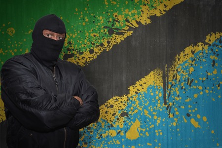 dangerous man in a mask standing near a wall with painted national flag of tanzaniaの写真素材