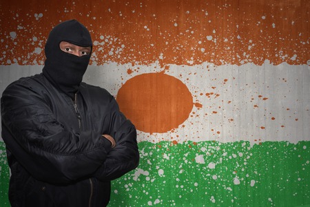 dangerous man in a mask standing near a wall with painted national flag of niger