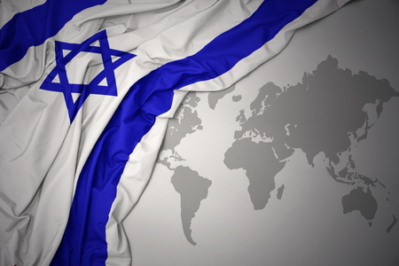 waving colorful national flag of Israel on a gray world map background.の写真素材
