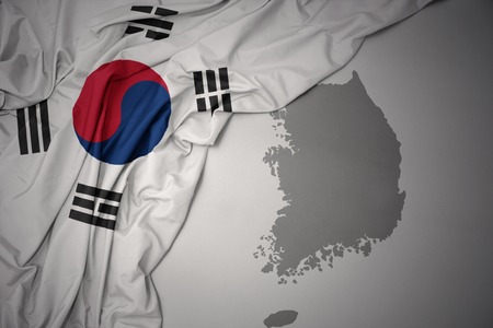 waving colorful national flag of south korea on a gray map background.の写真素材