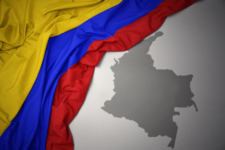 waving colorful national flag of colombia on a gray map background.の写真素材