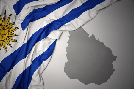 waving colorful national flag of uruguay on a gray map background.の写真素材