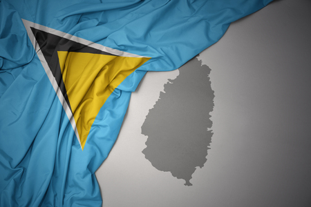 waving colorful national flag of saint lucia on a gray map background.の写真素材
