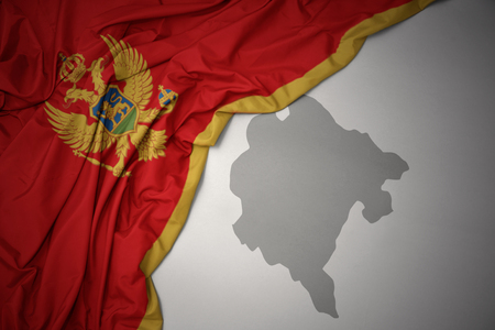 waving colorful national flag of montenegro on a gray map background.の写真素材