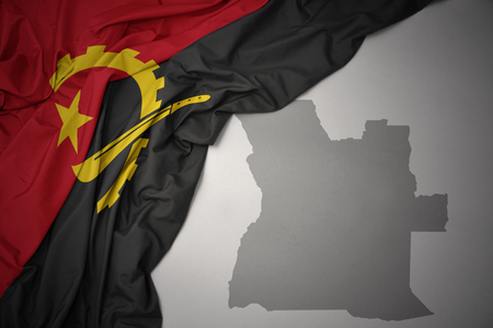 waving colorful national flag of angola on a gray map background. 3D illustrationの写真素材
