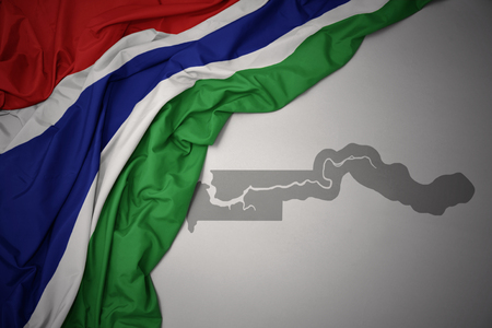 waving colorful national flag of gambia on a gray map background. 3D illustrationの写真素材