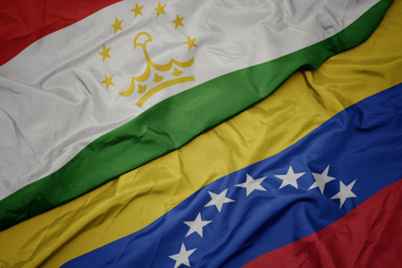 waving colorful flag of venezuela and national flag of tajikistan. macroの写真素材