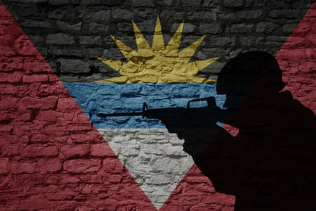 Soldier silhouette on the old brick wall with flag of antigua and barbuda country. Military strengthの写真素材