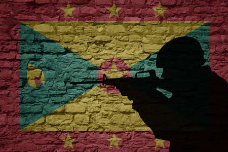 Soldier silhouette on the old brick wall with flag of grenada country. Military strength