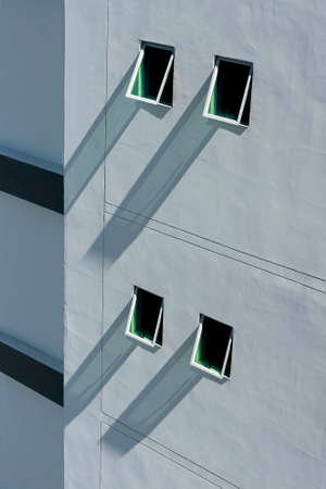 Four small windows with their long shadows on a tall wall.の写真素材
